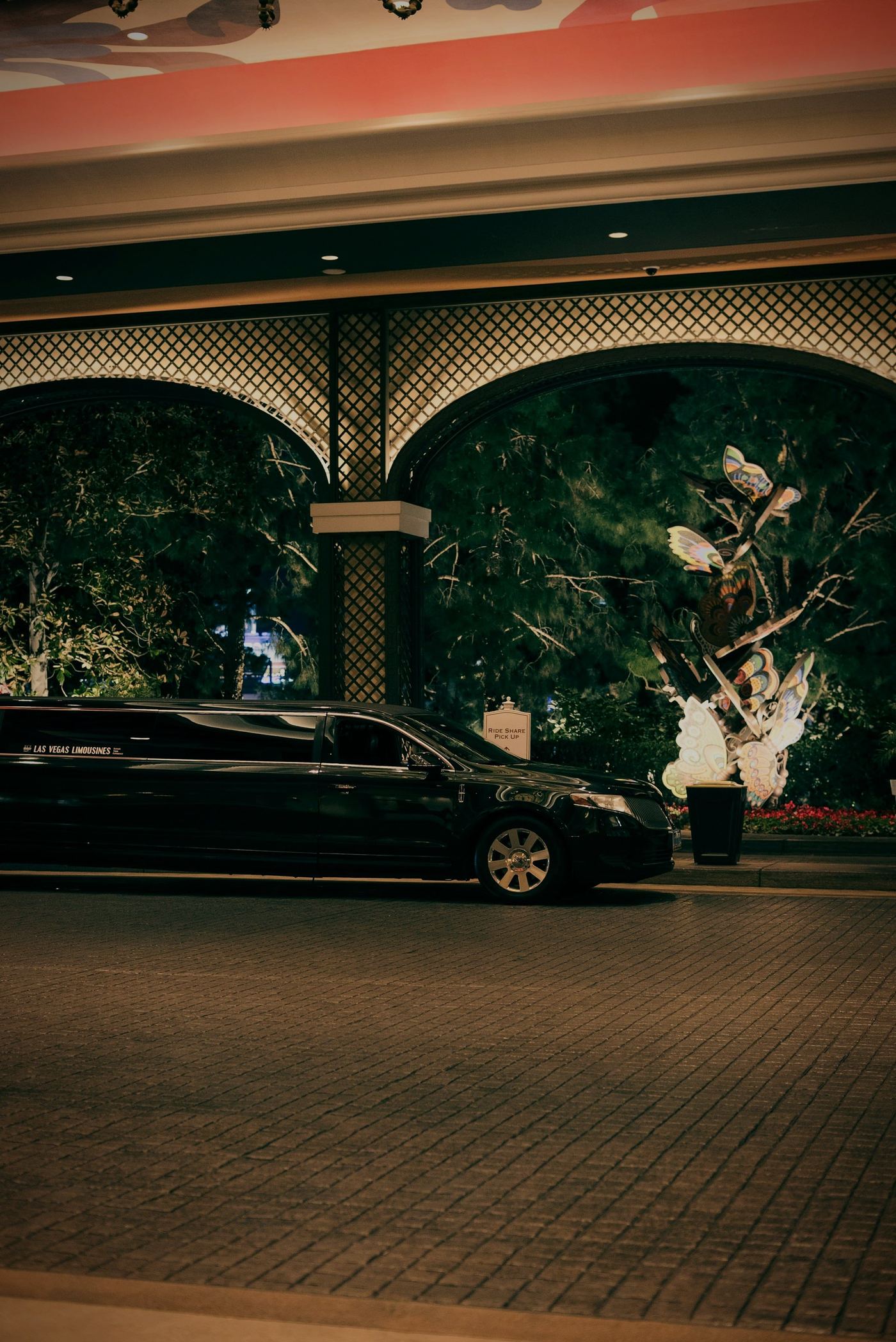 A black car waiting under a lit stone arch at night, the garden glowing behind it.