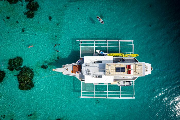 A catamaran from above, anchored over dark reef in turquoise water.
