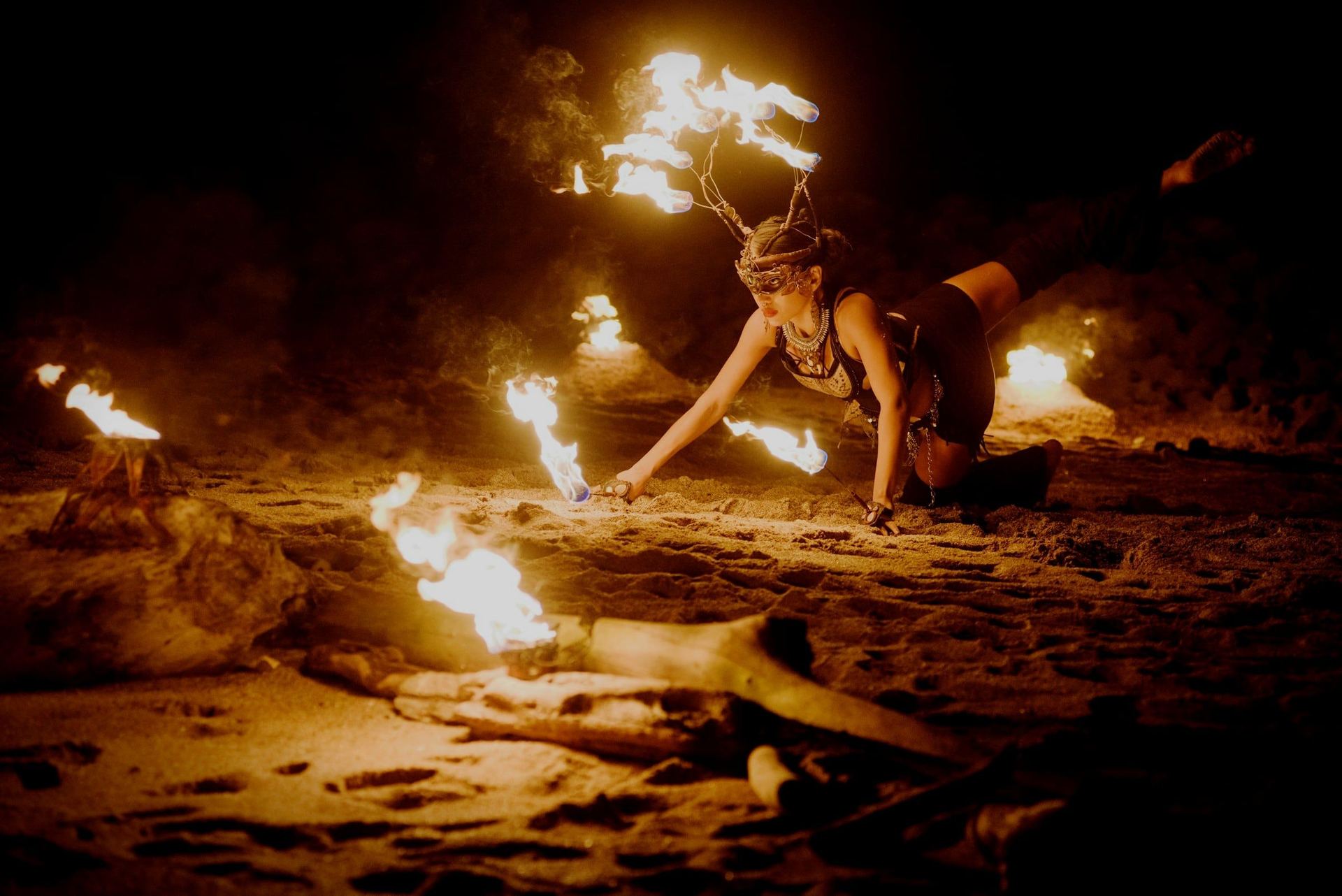 A fire dancer on the beach at night, flames trailing from her hands and crown.