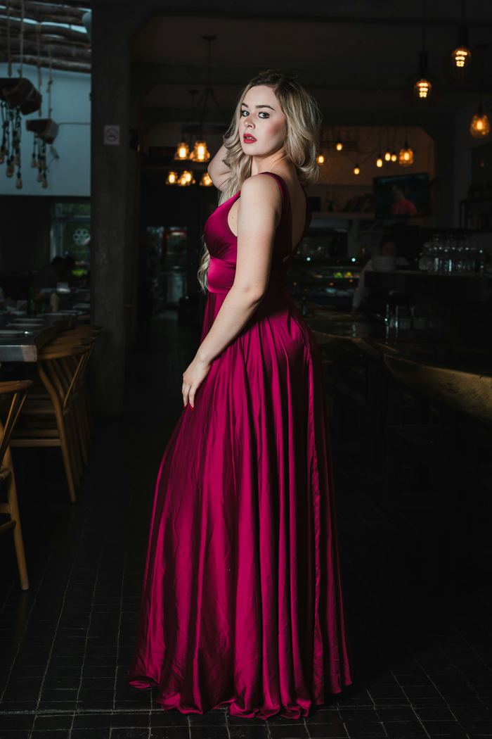 A guest in a long crimson gown at the bar, the room behind her in low light.