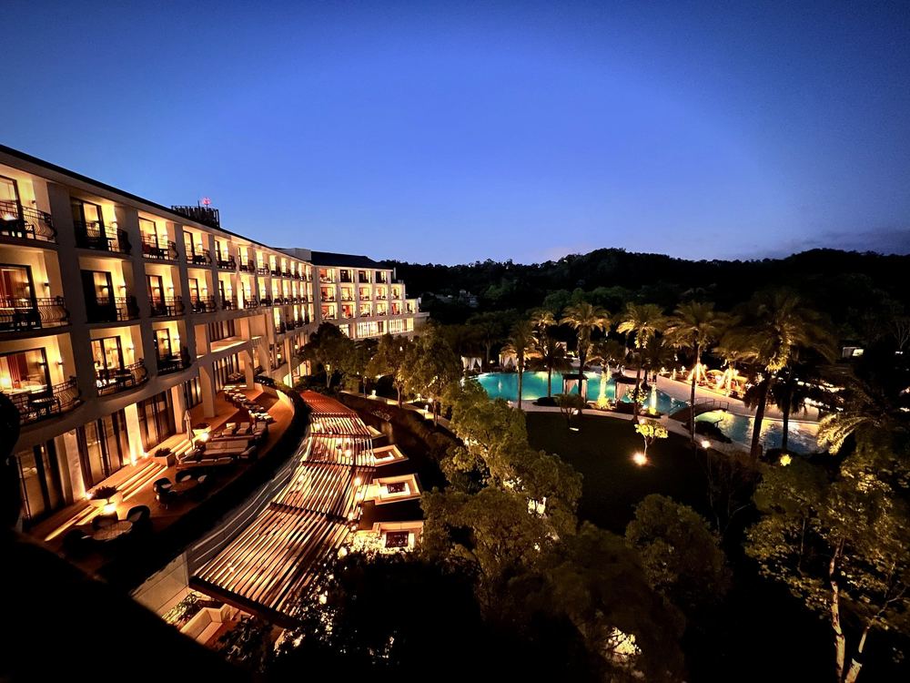 A resort building and pool lit gold at night, palms against a deep blue sky.