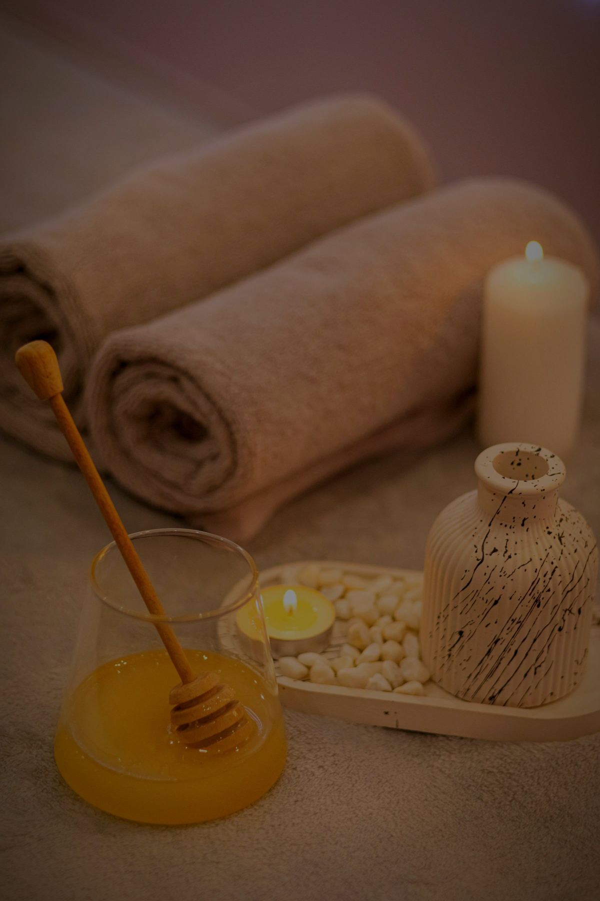 Rolled towels, a lit candle and a pot of honey on a stone ledge.