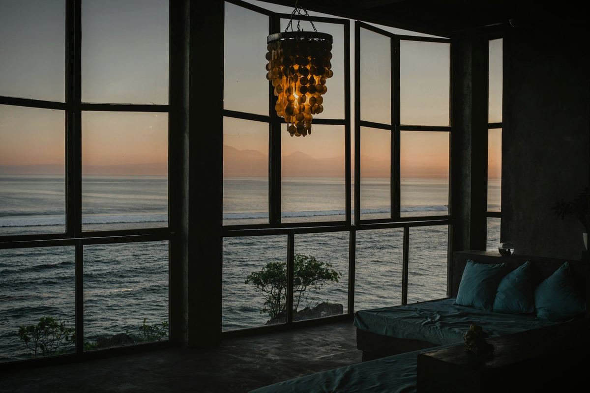 A dark room with a wall of glass onto the sea at sunset, a low sofa below the window.