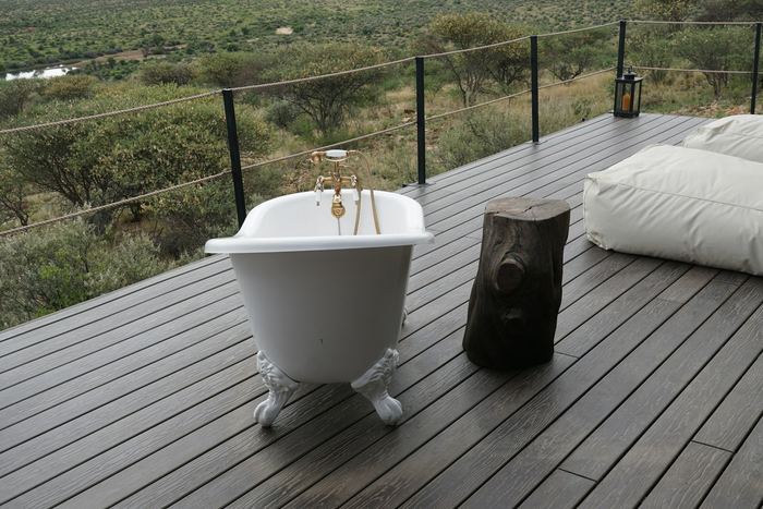 A white bath on a timber deck looking out over grassland.
