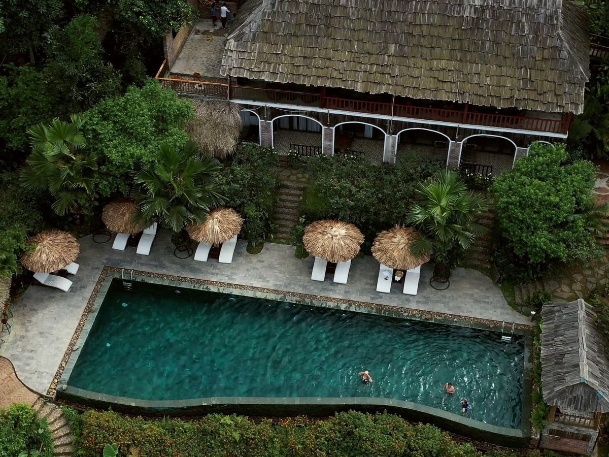 Aranya: a thatched lodge above its pool and shaded loungers in the forest, seen from the air.