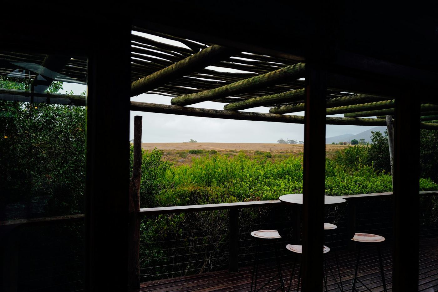 The view from a shaded timber deck out over green grassland, the posts framing the plain.