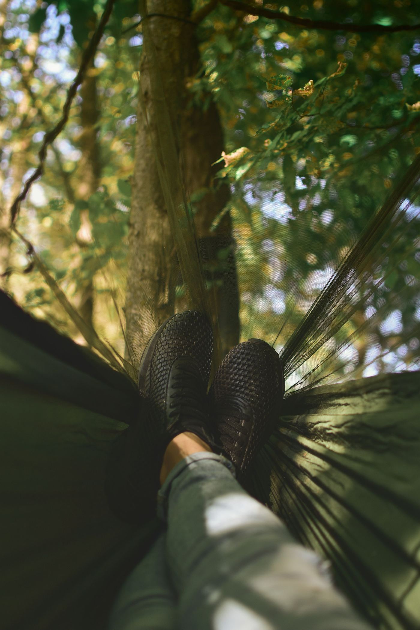 Boots crossed at the end of a hammock slung between trees, the forest light behind.