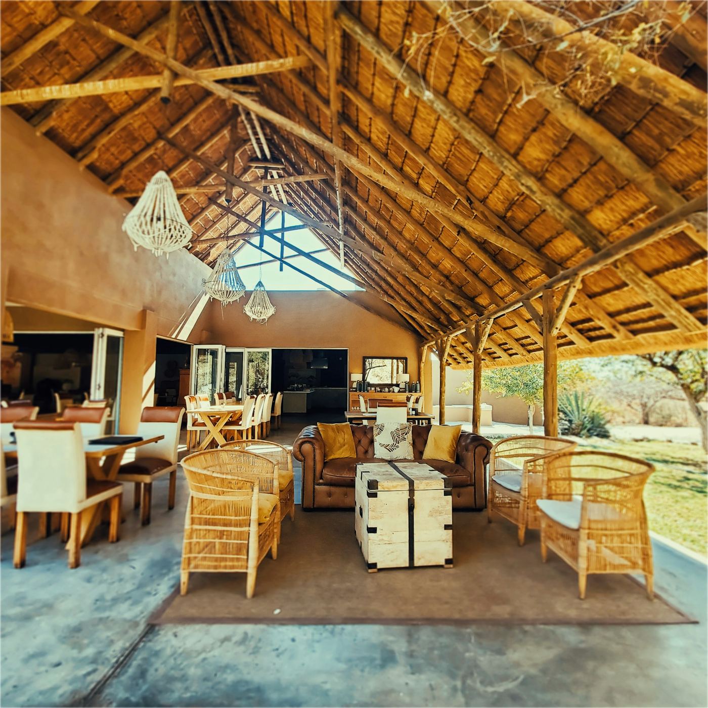 An open sided lodge under a high thatched roof, wicker chairs and leather sofas round a timber floor.