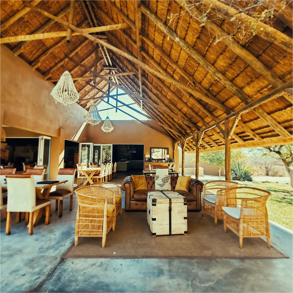 An open sided lodge under a high thatched roof, wicker chairs and leather sofas round a timber floor.