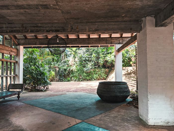 A cool stone floored veranda with a large clay pot, the garden bright beyond.