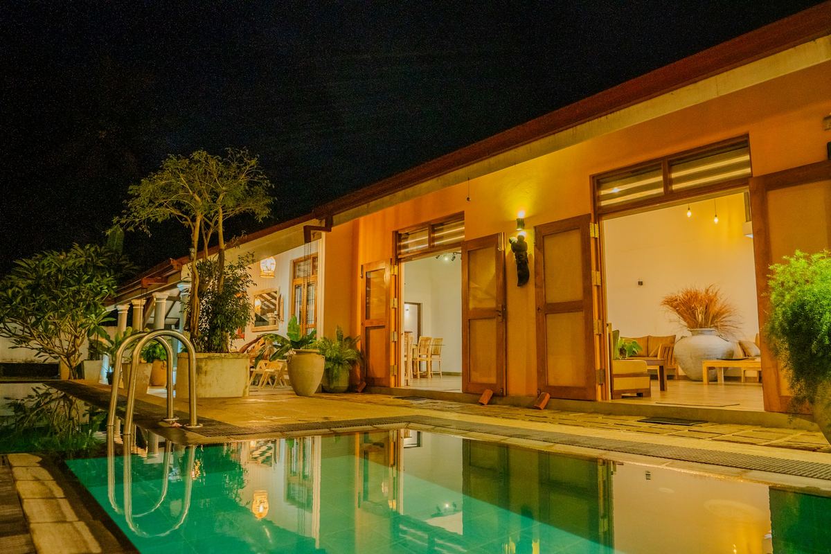 A villa’s pool lit after dark, its rooms glowing behind it.