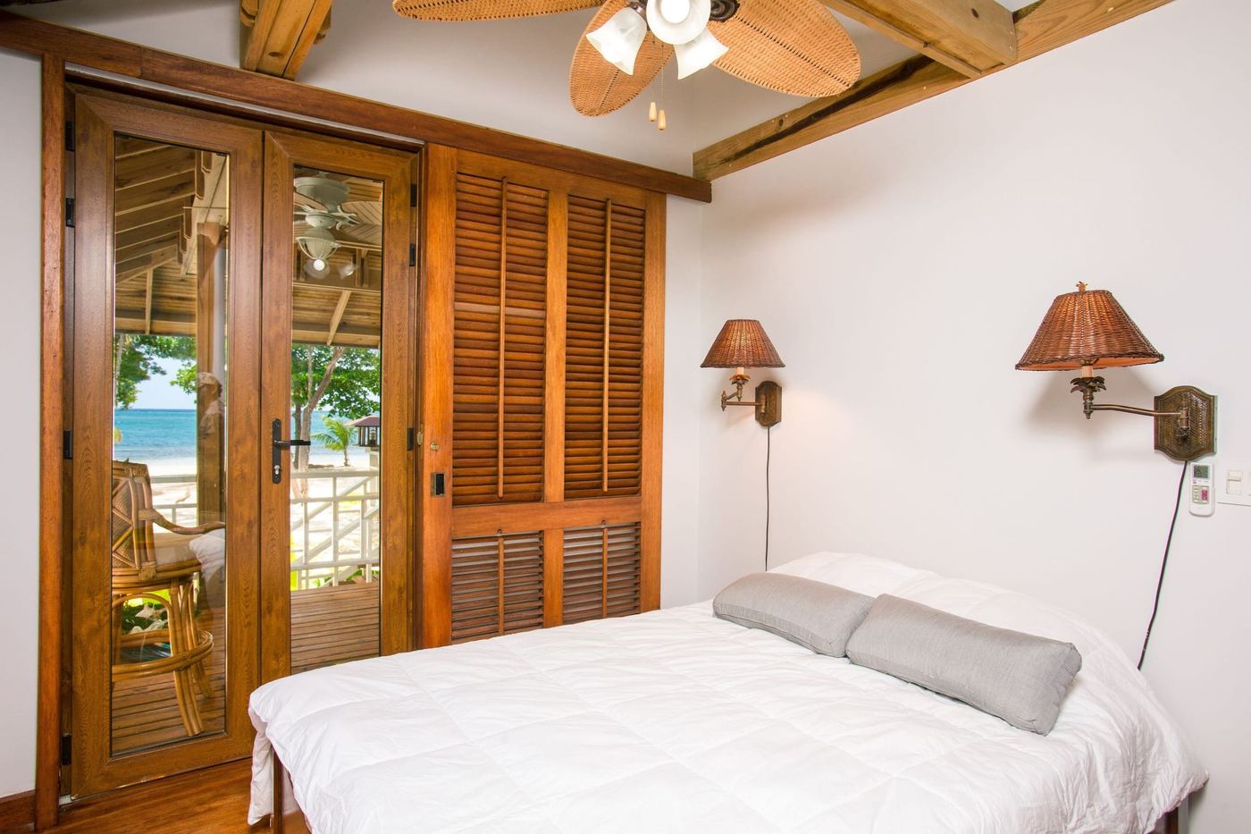 A white bedroom with louvred timber doors open to the sea.