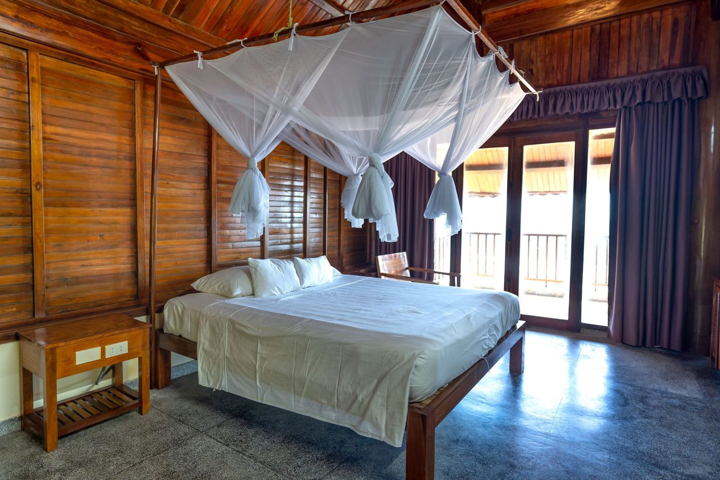 A timber walled bedroom with a four-poster under a white mosquito net.