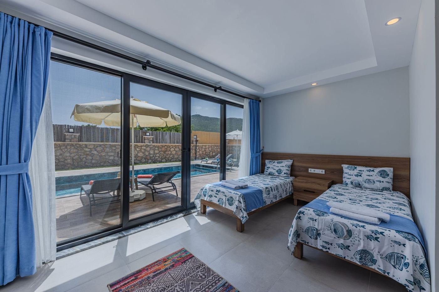 Twin beds by a glass wall, the pool and parasols outside.