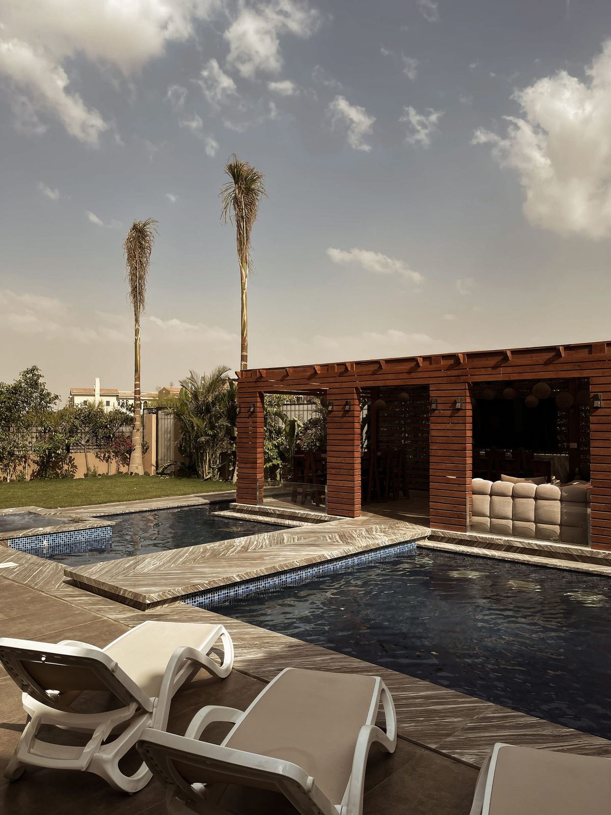 Gal House: the pool beside a timber pergola with built-in seats, loungers on the deck at dusk.