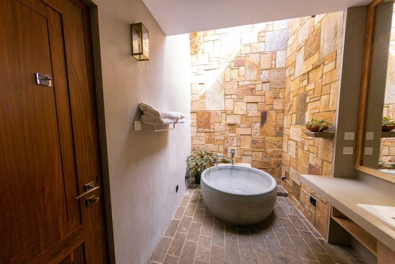 A round stone bathtub in an open air bathroom walled in warm sandstone.