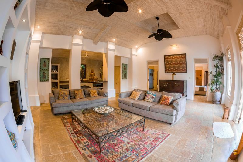 A high ceilinged lounge with patterned sofas, a carved chest and a ceiling fan.