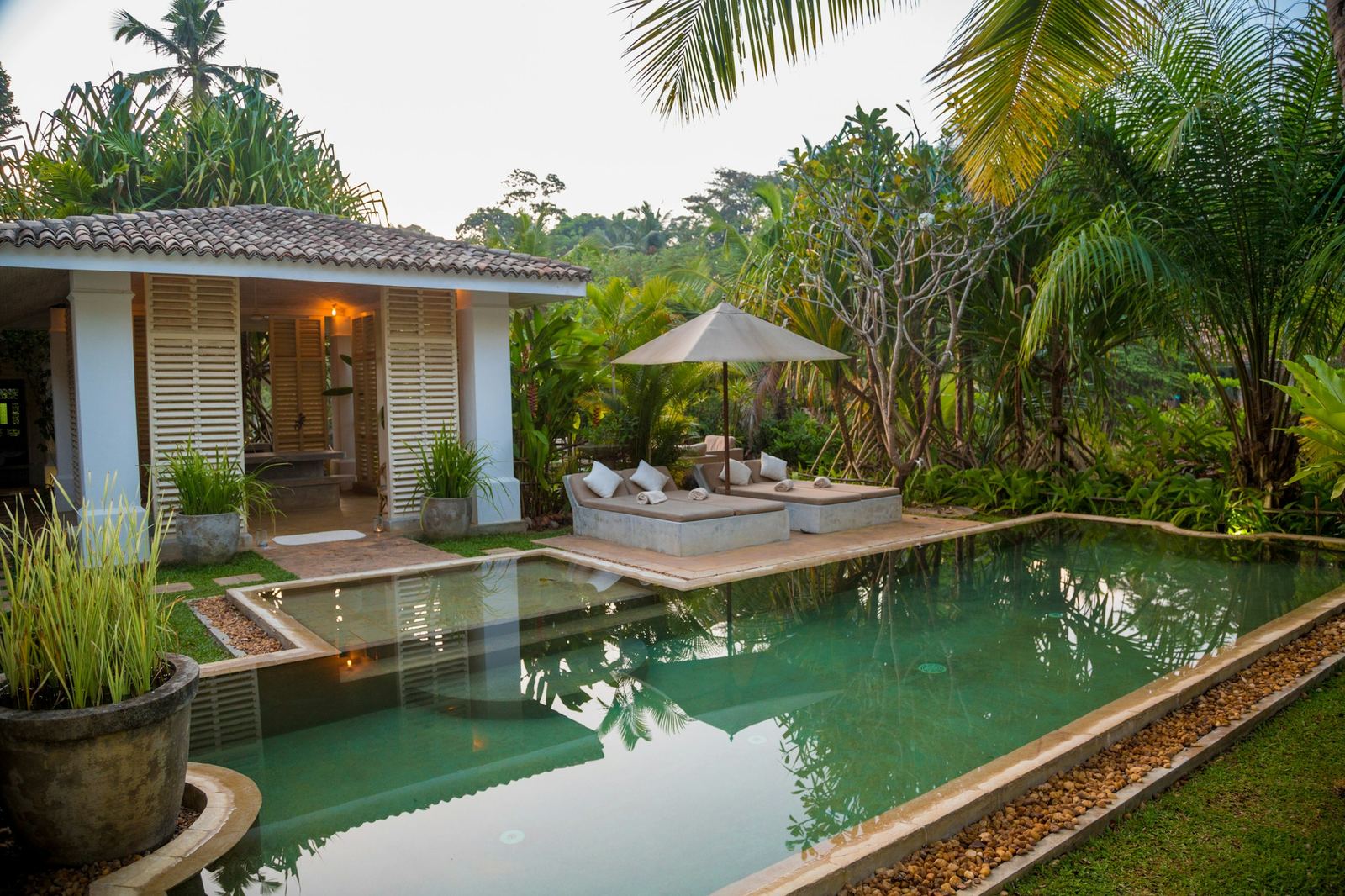 A white pool pavilion with a tiled roof beside a long, still swimming pool.