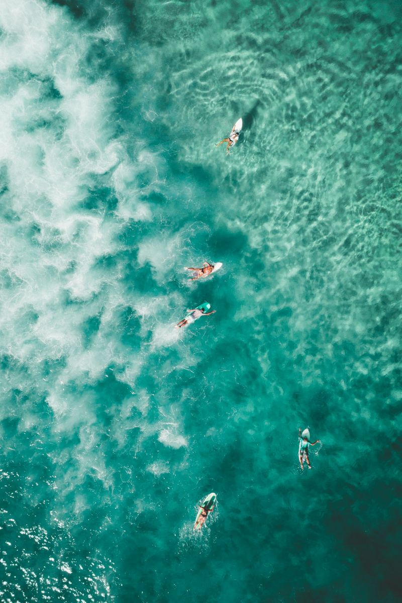 Two surfers paddling out through clear turquoise water, seen from above.