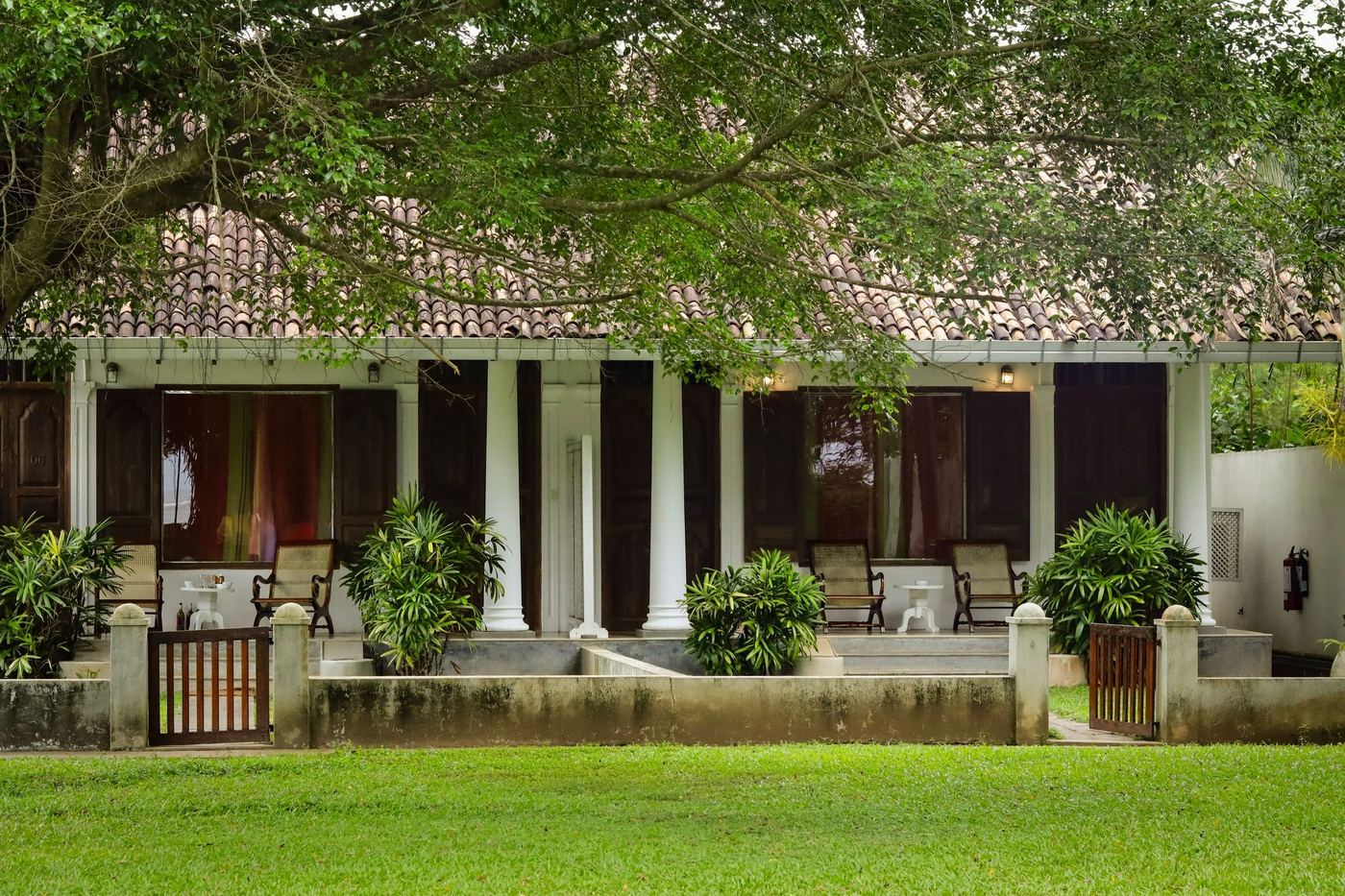 A colonial bungalow with a pillared verandah under a tiled roof, a lawn in front.