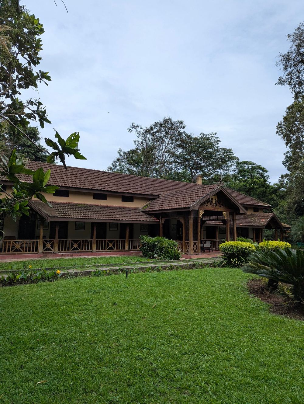 A long, low bungalow behind a wide lawn, trees all round.