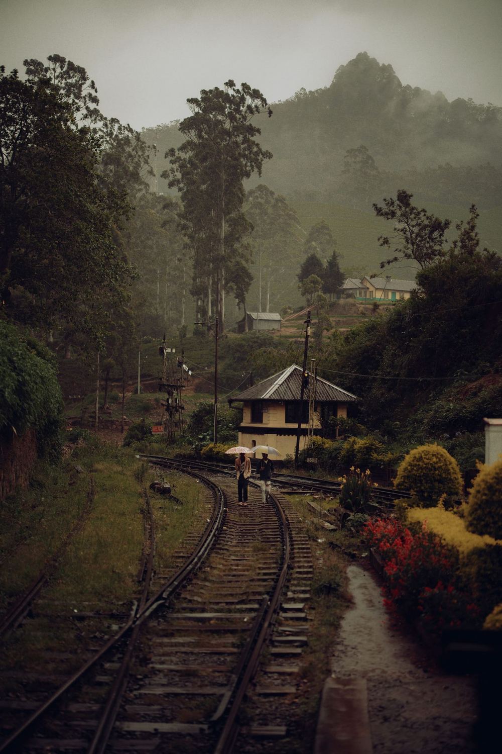 The railway curving through misty hills past a small station house.