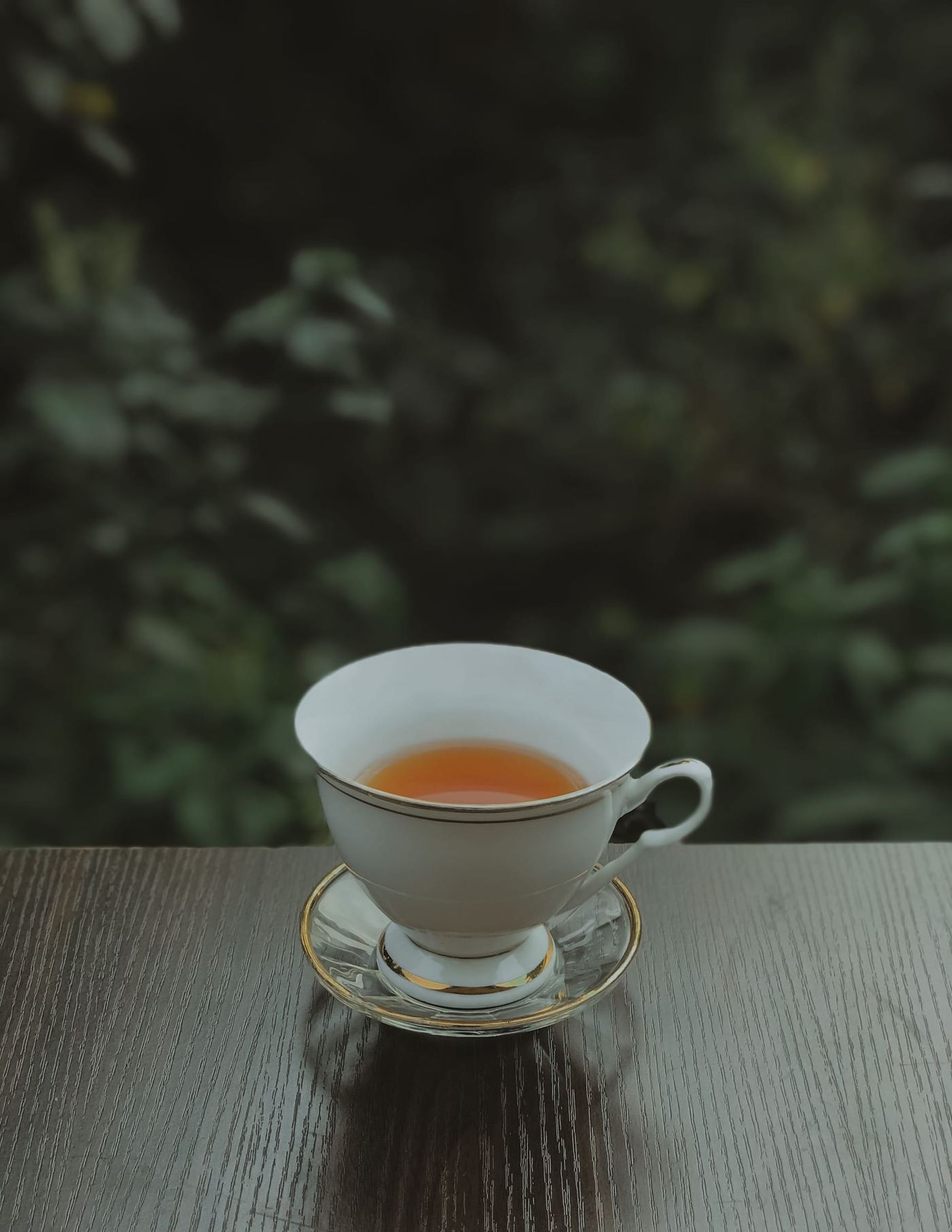 A cup of tea on a dark table, green leaves behind it.