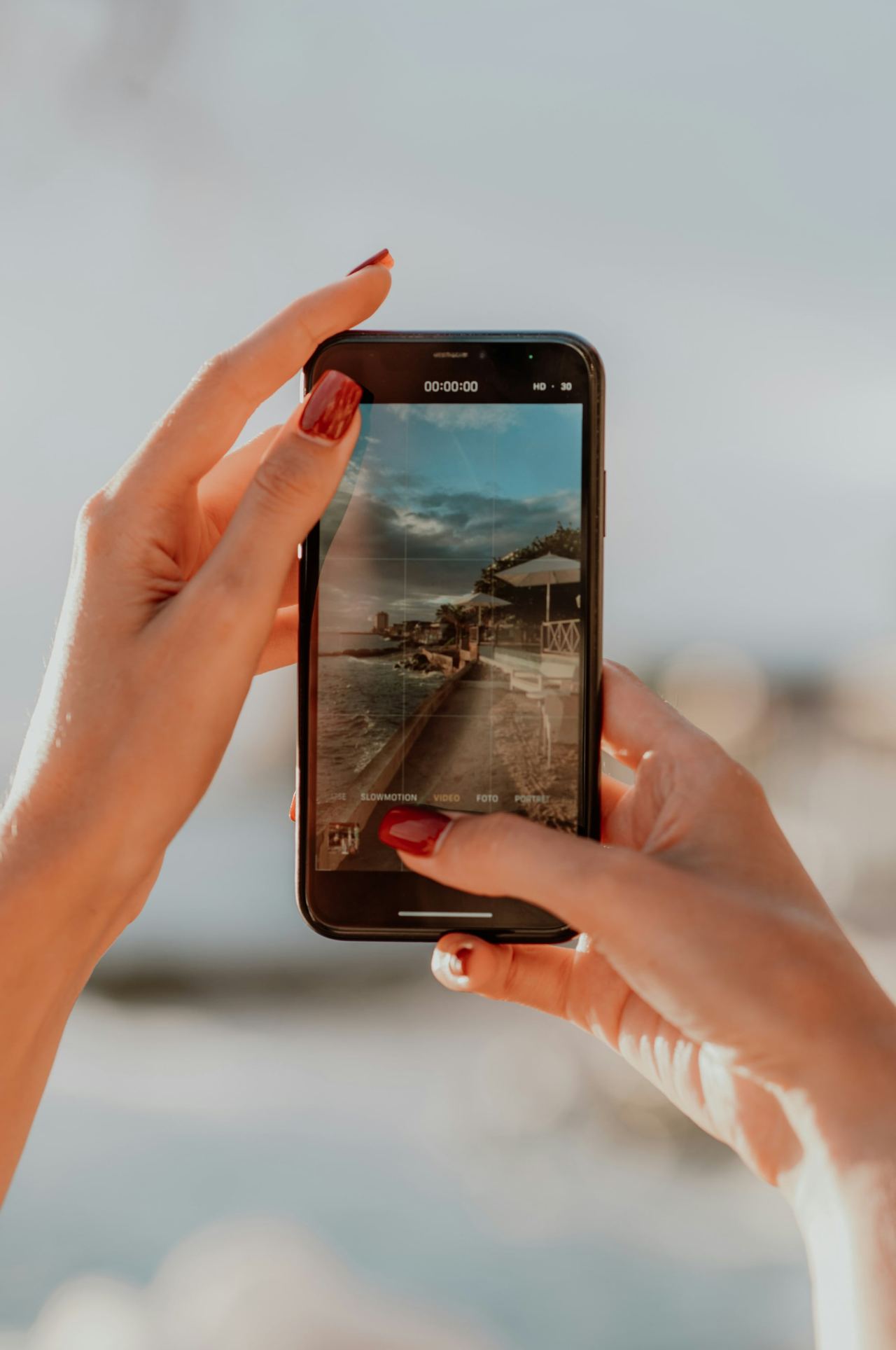 Two hands holding up a phone, filming a wooden pier over the sea.