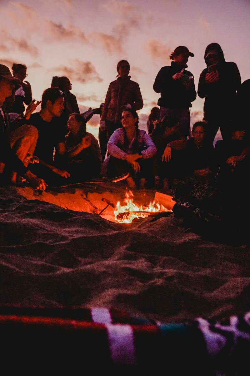 Friends sitting around a fire on the sand at night.