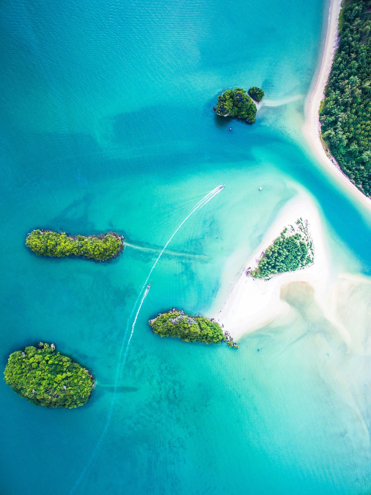 Small green islands and white sandbars in a shallow turquoise lagoon, from above.