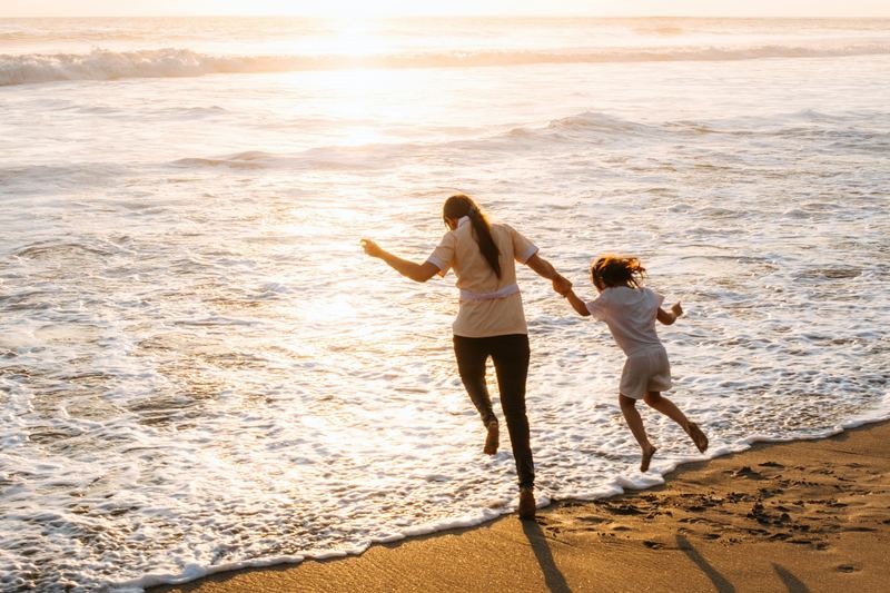A mother and her small daughter running hand in hand into the waves at sunset.