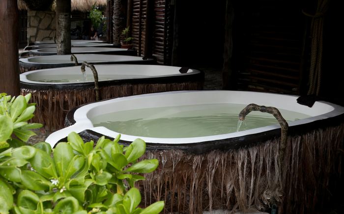 A deep stone tub on a timber deck, leaves at its edge and the light low.