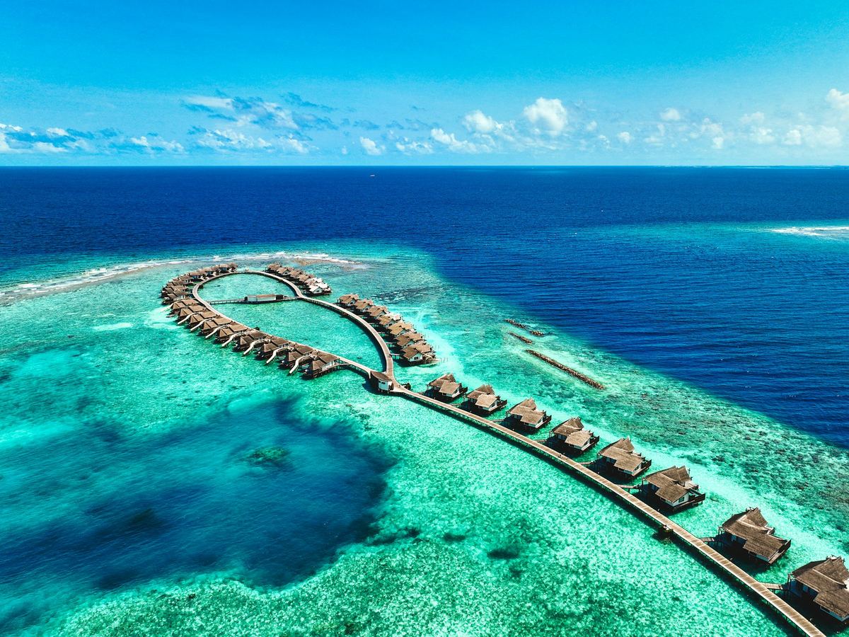 Villas on stilts curving out over a turquoise lagoon, seen from the air.