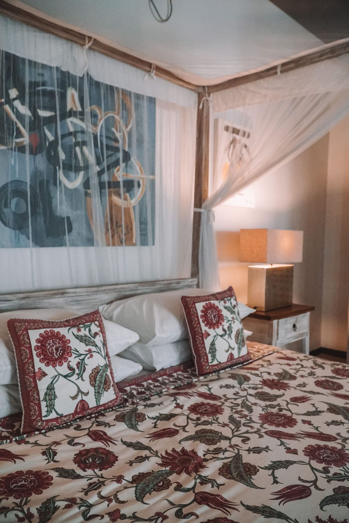 A bed with block printed red cushions and quilt, under a white mosquito net.