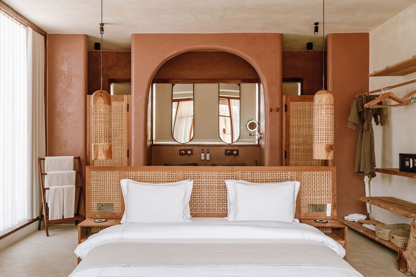 A bedroom with warm plastered walls and a mirror set in an arched alcove behind the bed.