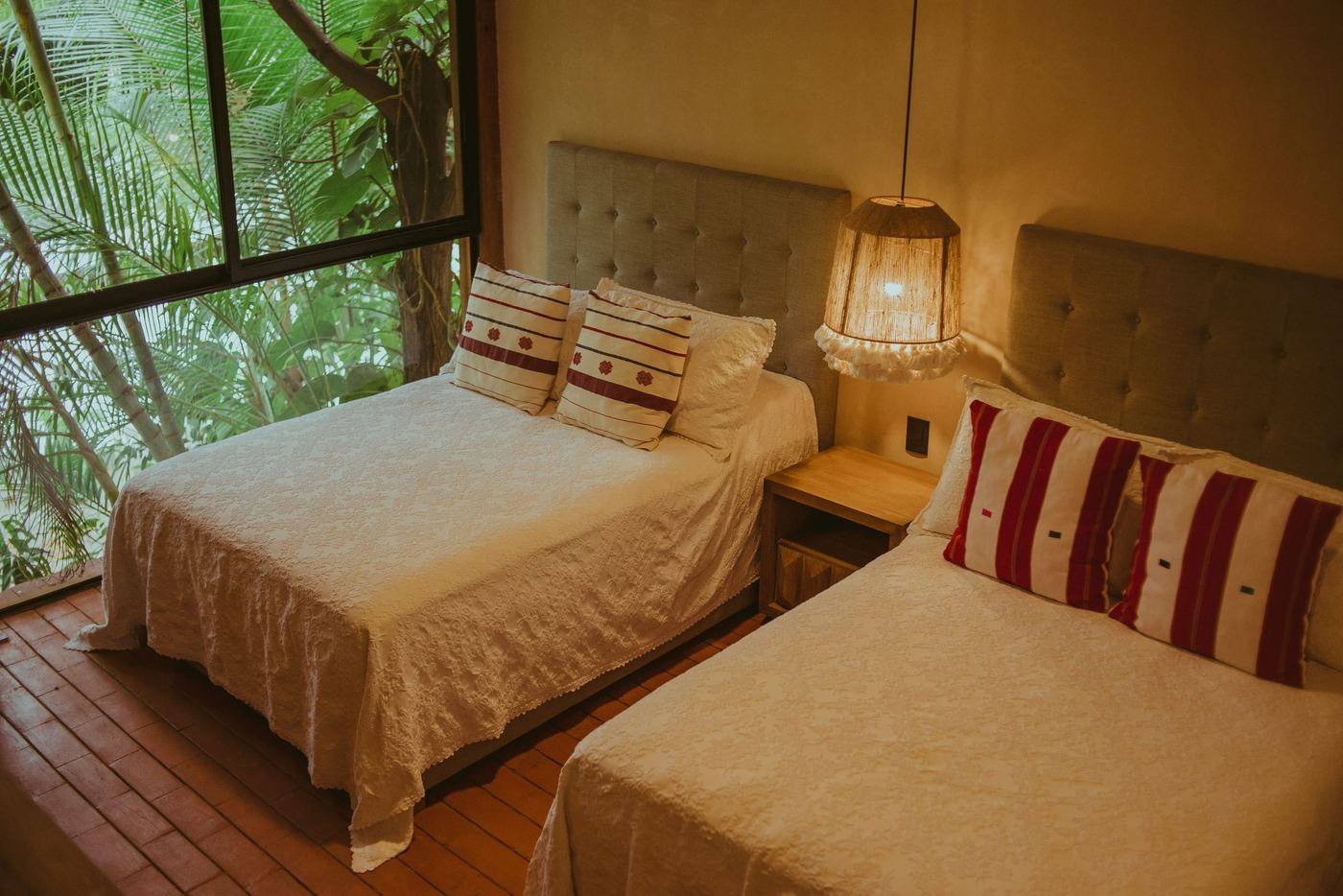 Twin beds with striped cushions, a window full of palm leaves beside them.