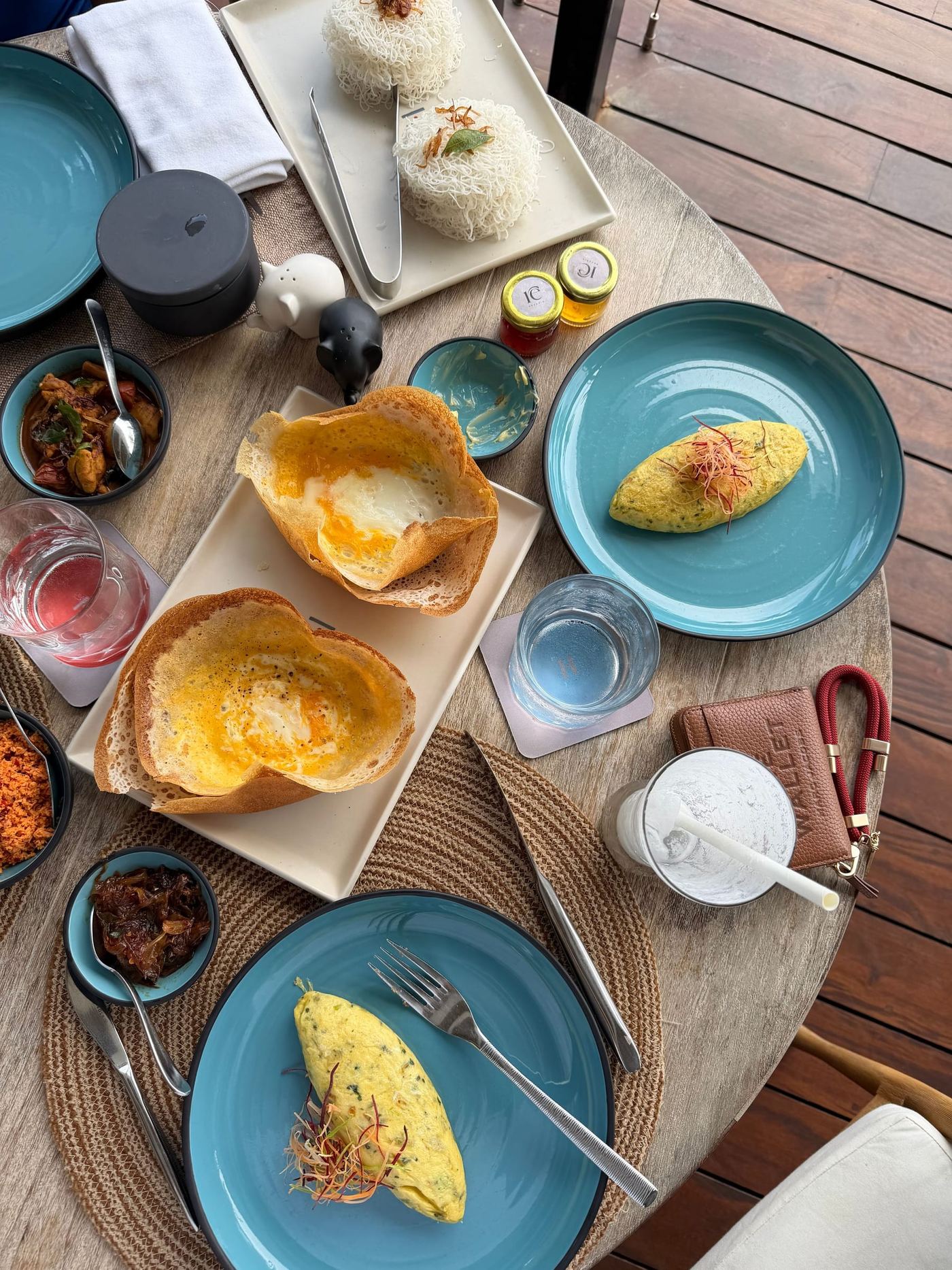 Breakfast on a timber table: egg hoppers, omelettes, curries in small bowls and tea.