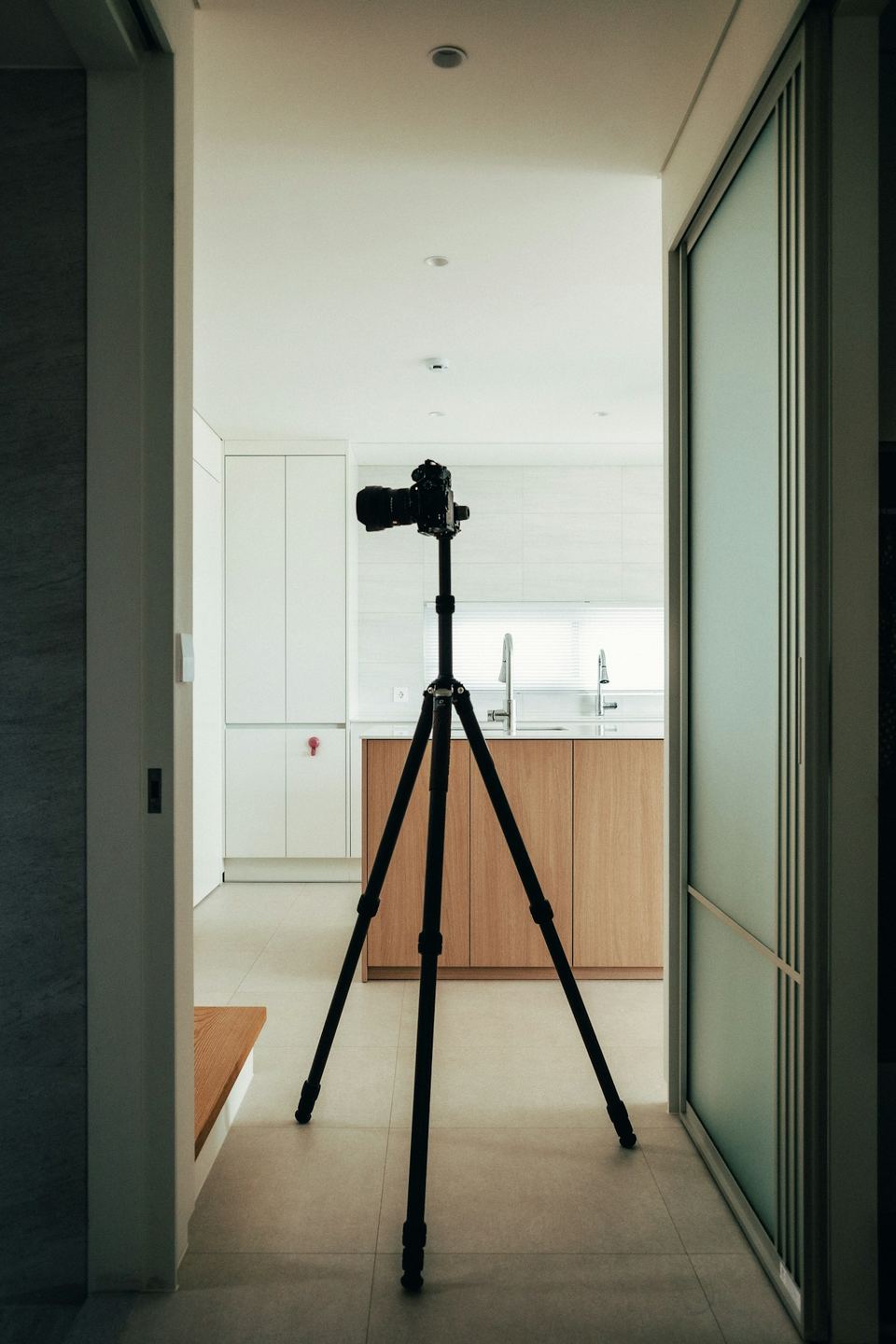 A camera on a tripod set up in the doorway of a bright interior.