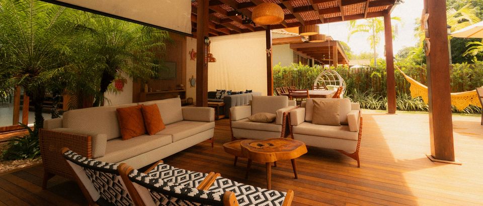 An open sided terrace lounge with timber floors, orange cushions and a garden beyond.