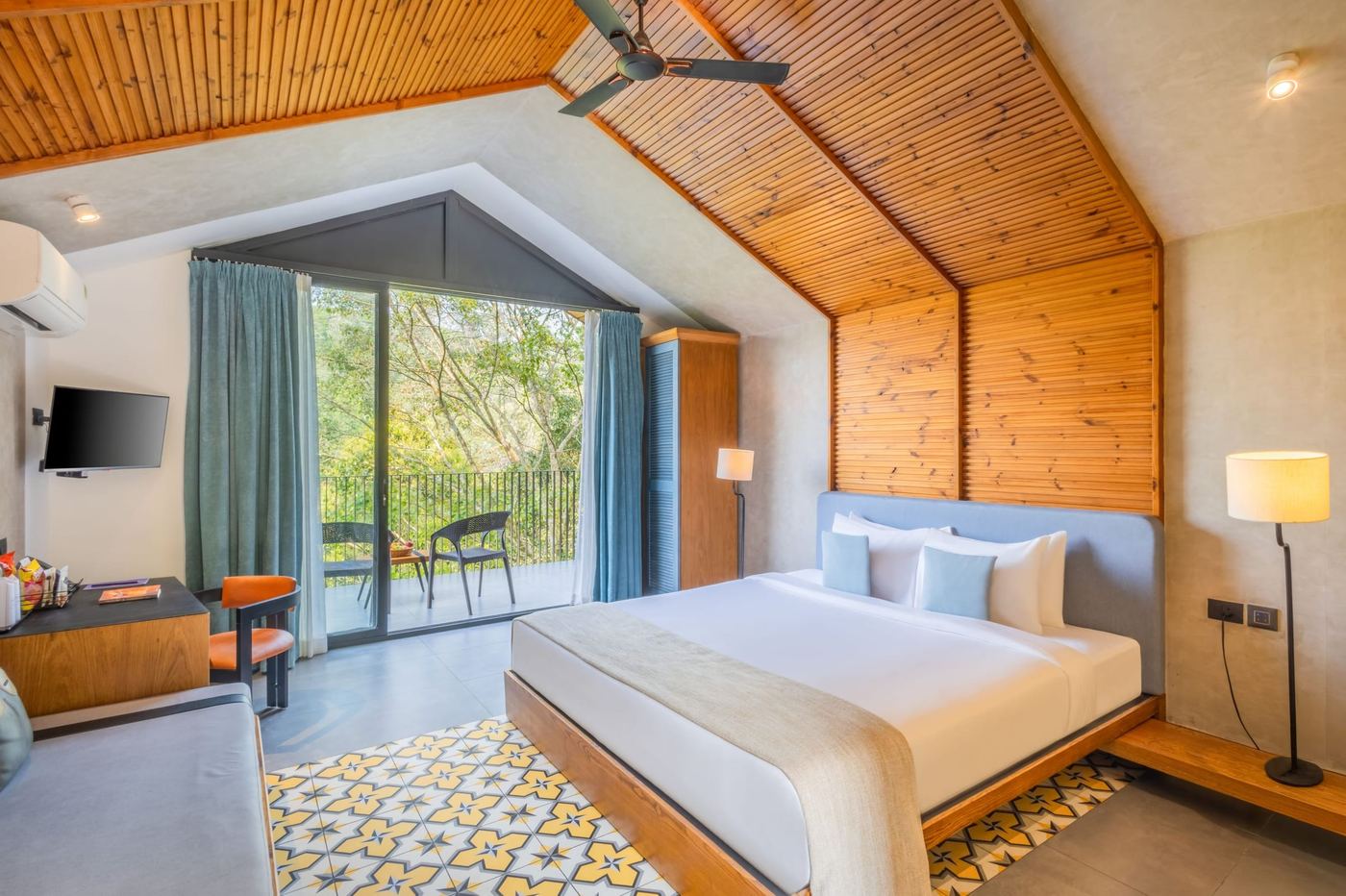 A bedroom under a pitched timber ceiling, a patterned tile rug and glass doors to the garden.