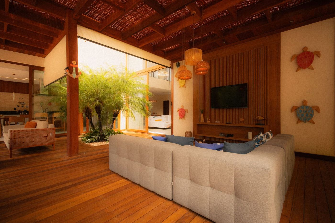 A living room panelled in timber, a long pale sofa and glass doors open to a garden.
