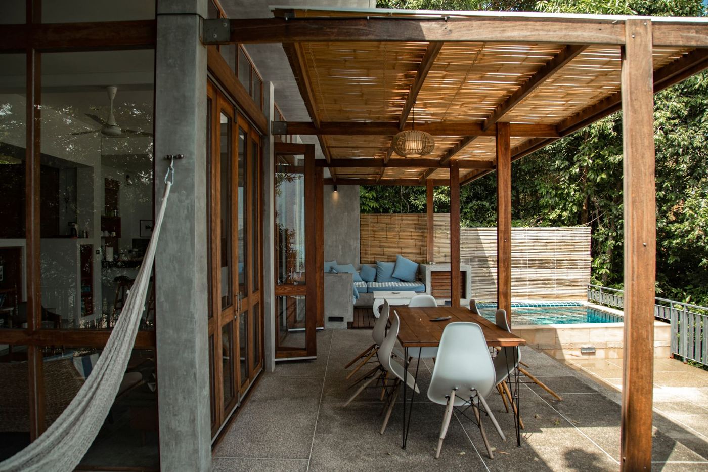 A terrace under a timber pergola: a hammock, a long table, and a small pool beyond.